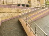 Podjazd dla niepełnosprawnych z poręczą, wykonany z cegły i płyt chodnikowych.