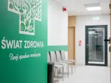 Zielona ściana z napisem "Świat Zdrowia", rząd krzeseł i drzwi w poczekalni kliniki.