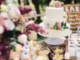 Elegancki tort weselny boho ozdobiony kwiatami, obok deserki i owoce.