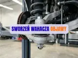 Widok na zawieszenie samochodu z widocznym sworzniem wahacza. Napis na zdjęciu informuje o objawach zużycia sworznia.