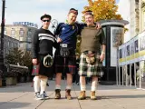 Trzech mężczyzn w tradycyjnych szkockich kiltach pozuje do zdjęcia na tle miejskiej zabudowy. Kto nosi kilt? Ci panowie!