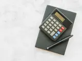 Kalkulator i długopis na czarnym notesie. Czas obliczyć, ile urlopu na pół etatu przysługuje.