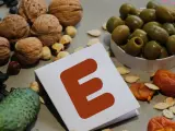 Orzechy, pestki, oliwki i suszone morele wokół kartki z literą "E" symbolizują bogactwo witaminy E.