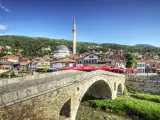 Kamienny most nad rzeką, z widokiem na meczet i miasto na wzgórzu. Kosowo atrakcje turystyczne zachwycają.