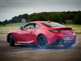 Czerwona Toyota 86 GR w poślizgu, z opon dymiących na asfalcie. W tle zielone pola i drzewa.
