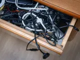 Szuflada pełna plątaniny kabli, ładowarek i urządzeń elektronicznych.