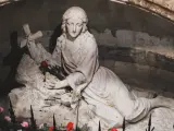 A stone sculpture depicts the serene body of Mary Magdalene, resting with a cross and a single red rose.