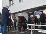 Grupa ludzi stoi przed budynkiem spółdzielni mieszkaniowej w deszczu, niektórzy pod parasolem.