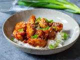 Krispig koreansk kyckling med sesamfrön och salladslök serveras på en bädd av vitt ris i en skål.
