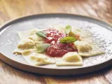 Pyszne raviolini z sosem pomidorowym i parmezanem, ozdobione listkami szałwii, na szarym talerzu.