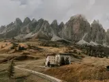 Malownicze **Val di Funes** z górami w tle, hotel na wzgórzu i kręta droga.