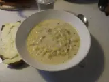 En krämig fänkålssoppa med potatis serveras i en vit skål, bredvid en bit rostat bröd med ost.