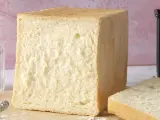 Un pain de mie moelleux, parfait pour une recette facile. Un pot de farine et un moule à pain sont à proximité.