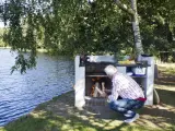 Man tänder en brasa i en nybyggd grill av tegelstenar vid en sjö.