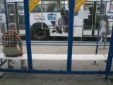 Mężczyzna czeka na przystanku na autobus 102. Rozkład jazdy jest niewidoczny, ale widać autobus z reklamą Allegro.