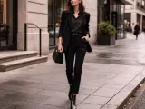 Elegancka kobieta w czarnym garniturze, z torebką i butami, idzie ulicą. Jej styl to nowoczesny goth.