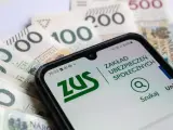 Zasiłek macierzyński 80 czy 100% i 60%? Telefon z aplikacją ZUS na tle polskich banknotów.