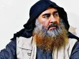 Mężczyzna z długą, siwiejącą brodą i czarnym nakryciem głowy, przypominający Abu Bakra al-Baghdadiego, siedzi w jasnym ubraniu.