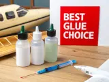 Three bottles of model glue and a syringe sit on a wooden surface next to model airplanes. A red sign reads "BEST GLUE CHOICE.