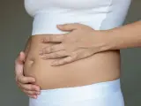 Dłońmi obejmuje zaokrąglony, napięty brzuch, który wygląda jak wzdęty.