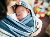 Ein Baby schläft friedlich in einem blauen Tragetuch. Der sanfte Tagesrhythmus des Babys wird durch die Nähe zur Mutter unterstützt.