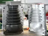 Two halves of a mold for compression molding products, one showing a black bellows-like component, the other an empty cavity.