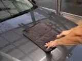 Hände trocknen mit einem Mikrofasertuch die Motorhaube nach der Autowäsche. Perfekt für das auto innenraum trocknen.