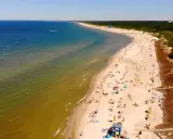 Słoneczna plaża na Litwie, gdzie turkusowe morze łagodnie przechodzi w zielonkawe wody. Tłumy plażowiczów odpoczywają na piasku, ciesząc się letnim dniem.