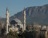 Imponujący meczet z minaretami, górujący nad budynkami stolicy Albanii, na tle skalistych gór.