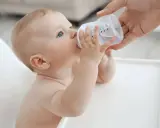 Niemowlę pije wodę z butelki. Od kiedy dziecko może pić wodę mineralną nieprzegotowaną? Od 6. miesiąca życia, gdy zaczyna rozszerzać dietę.