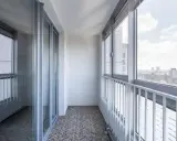 Zabudowanie balkonu w bloku z widokiem na miasto. Szklane drzwi i okna tworzą przytulną przestrzeń.
