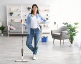 Uśmiechnięta kobieta z mopem w ręku, gotowa do mycia podłogi w jasnym salonie.