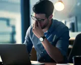 Mann reibt sich erschöpft die Augen vor dem Laptop. Ein Hackerangriff auf Privatpersonen kann zu solchen Belastungen führen.