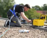 Mann mit Absturzsicherung führt Flachdach Leckageortung mit Messgerät durch.