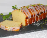Ein saftiger mallorquinischer Zitronenkuchen mit Zuckerguss und Pistazien, daneben ein angeschnittenes Stück.