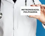 Lekarz w białym kitlu trzyma kartkę z napisem "METRONIDAZOL POLPHARMA". Metronidazol bez recepty to lek, który może pomóc w leczeniu infekcji.