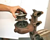 Dłoń trzyma rozłożoną turbosprężarkę, wskazując na uszkodzona turbina objawy. Rdza i luźne części sugerują problemy.