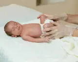 Delikatne badanie niemowlaka, ocena symetrii kończyn. Dłoń w rękawiczce delikatnie dotyka nóżek dziecka.