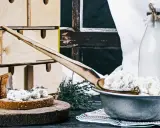 Fromage blanc frais, parfait pour une recette fromage blanc yaourtière. Servi sur du pain avec des herbes, à côté d'une bouteille de lait.