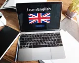 Laptop z napisem "Learn English" i flagą Wielkiej Brytanii. Obok kawa, notatnik i roślina. Idealne do nauki fce use of english.