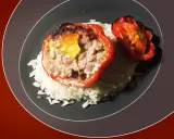 Poivrons rouges farcis à la viande, servis sur un lit de riz blanc. Une sauce légère accompagne ce plat, rappelant les saveurs des tomates farcies.