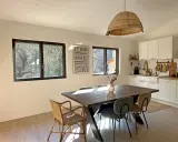 Comedor y cocina luminosos con mesa de madera, sillas de mimbre y tapizadas, y ventanas de cristal térmico que dejan ver el exterior.