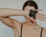 Dłoń z czarną taśmą w kształcie krzyża zakrywa oko, symbolizując traumę seksualną i potrzebę ochrony.