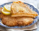 Due cotolette al forno dorate e croccanti, servite su un piatto blu e bianco con spicchi di limone.
