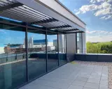 Moderne Dachterrasse mit Glasfront und Lamellendach. Ein gelber Schlauch liegt bereit, um das Flachdach anzuheben und zu pflegen.