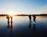 Silhuetter av skridskoåkare med stavar och ryggsäckar på en spegelblank is vid solnedgången. En magisk upplevelse av skridskoåkning i Stockholm.