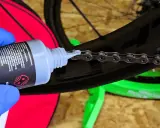 Blaue Handschuhe tragen, um die Fahrradkette wachsen zu lassen. Ein Tropfen Öl fällt auf die Kettenglieder.