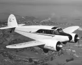 Ein weißes, zweimotoriges hochdecker flugzeug fliegt über eine Stadt und Industrieanlagen.