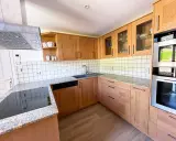 Cuisine en bois clair, avec des placards vitrés rappelant l'intérieur d'un voilier. Le plan de travail en granit et les appareils modernes complètent ce décor chaleureux.