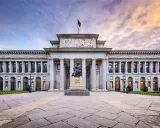 Das Prado Museum in Madrid, ein Meisterwerk der Architektur, mit einer Statue davor und einem dramatischen Himmel.